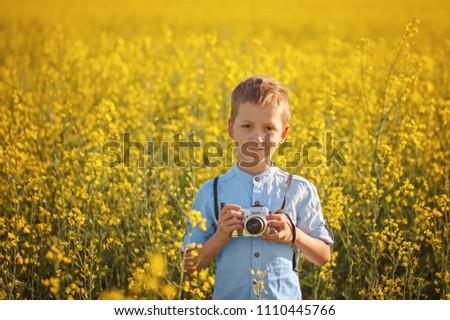 Portrait of little boy photographer with camera on sunset yellow field background.