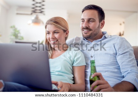 Picture of young happy couple sitting on sofa at home.Looking happy,using laptop computer.