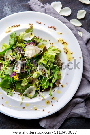 Healthy lettuce arugula salad with edible flowers and microgreens on white plate, dark background. Top view.