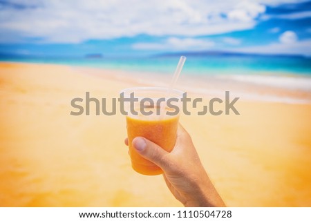 Healthy juice smoothie juice drink selfie on beach. Turmeric, carrot, papaya or orange fruit, Man hand holding plastic cup on beach summer background. Food picture of tropical fruits diet lifestyle.