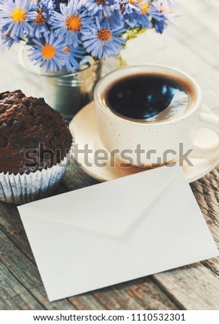 photo of sunny morning - chocolate muffin, cup of coffee and a bouquet of blue flowers and an envelope.
