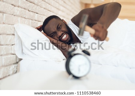 African American man is hammering alarm clock. Waking up.
