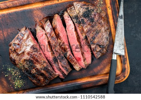 Barbecue dry aged wagyu flank steak sliced as top view on a burnt cutting with a knife Royalty-Free Stock Photo #1110542588