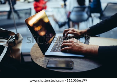 Cropped image of man while typing on laptop computer, installing application, publishing article on online banking website and updating software on netbook connected to wireless internet at cafe
 Royalty-Free Stock Photo #1110556199