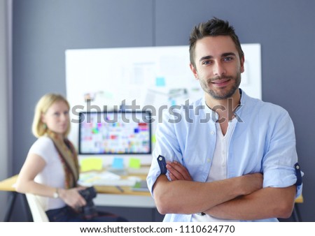 Portrait of young designer in front of laptop and computer while working . Assistant using her mobile at background