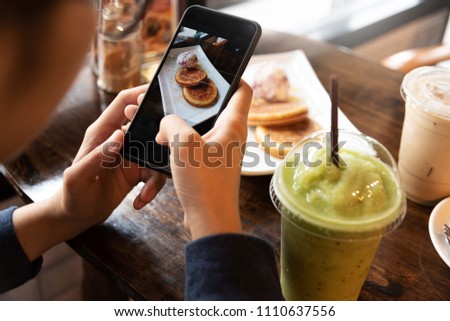 Close up Female hands taking cake, cup of coffee and green tea pictures with smart phone on wood table at the cafe.
