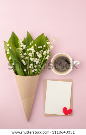 Coffee mug with bouquet of flowers lily of the valley and blank with red heart oj pink pastel background, beautiful breakfast, vintage romantic card, top view, flat lay