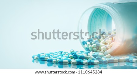 Blue and white capsules pill spilled out from white plastic bottle container. Global healthcare concept. Antibiotics drug resistance. Antimicrobial capsule pills. Pharmaceutical industry. Pharmacy. Royalty-Free Stock Photo #1110645284