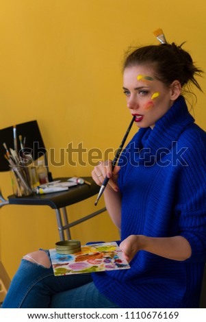 Girl artist paints sunflowers oil paints on canvas. She is wearing blue sweater. Woman is holding brush and palette with paints. She reflects.