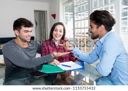 Young caucasian love couple receiving key for new house indoor with real estate agent