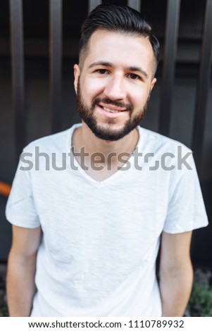 Portrait of a stylish hipster Guy, in a white blank t-shirt, on a black fence background,