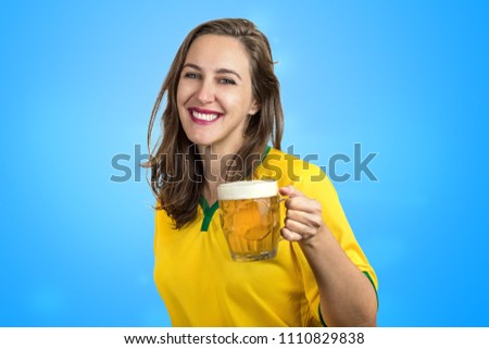 Woman cheering for Brazil and drinking cold beer in the cup in the cup. Brazilian girl  fan celebrating with beautiful smile on blue background.