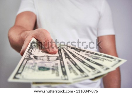 A young man holding a five dollar bill, giving it - on a white background