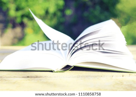 Open book with pages flipped by the wind, on wooden table. Green bokeh on the background.