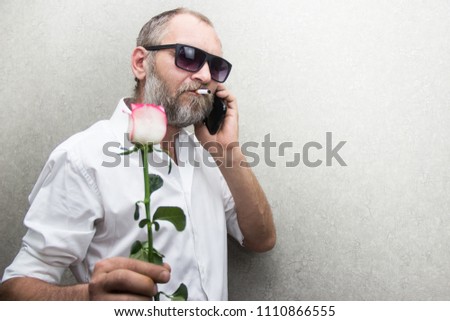 brutal man in glasses with a beard and a cigarette holds a rose in his hands