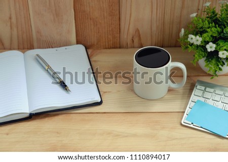 Coffee mug on wooden table and computer keyboard with notepad paper.
