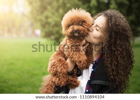 Happy woman with little dog, outdoors portrait at city park background. Two beautiful curlies posing and kissing, copy space