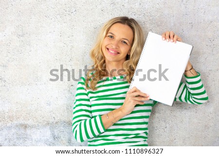 young pretty woman with striped pullover holding blank, checkered paper block in the camera