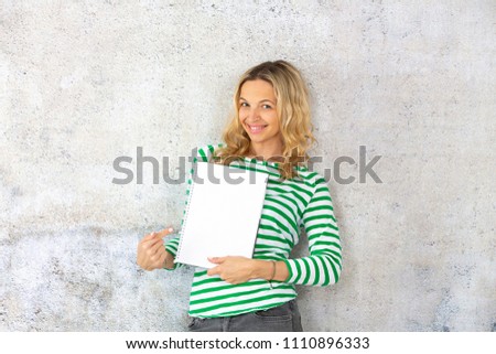 young pretty woman with striped pullover holding blank, checkered paper block in the camera
