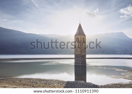 Old church tower in water at sunset. Resia Lake (Lago di Resia or Reschensee) in South Tyrol, Italy.