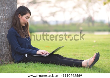 Young businesswoman sitting in park working on  notebook. Outdoors work and relaxation concept