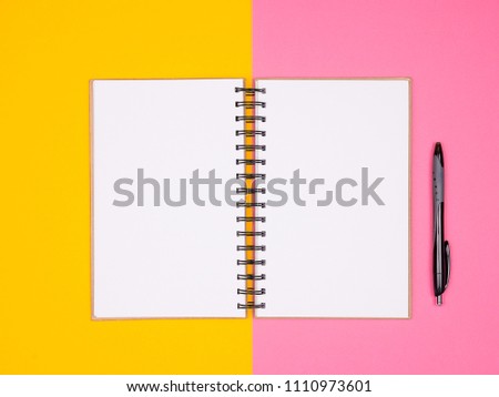 Open paper notebook next to a pen on two colored background in studio photo. Top flat lay view. Pastel colors
