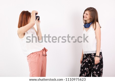 Woman photographer and her female friend taking pictures in studio over a white wall