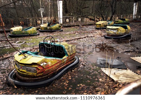 Old broken rusty metal radioactive yellow cars, children's electric cars, abandoned among vegetation, the park of culture and recreation in the city of Pripyat, the Chernobyl disaster, Ukraine. Royalty-Free Stock Photo #1110976361