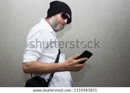 A man in a shirt with a beard wearing glasses and a hat talking on his cell phone