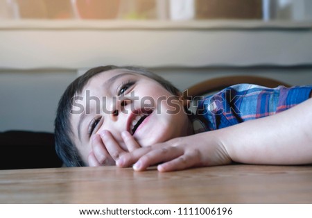 Cute little boy playing hide and seek on the table while waiting for food in the coffee shop, Happy kid puting his head down on the table and looking up with smiling face
