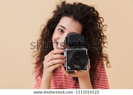 Image of pretty young curly woman photographer isolated over beige background holding camera.
