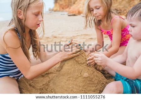 Brother and sisters are playing with sand on the beach. Build castles from sand. Lifestyle photo