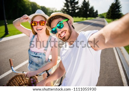 Self portrait of cheerful stylish brother and sister shooting selfie on front camera outdoor while riding on bikes enjoying holidays. Sun adventure photography concept