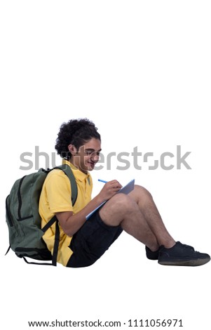 Young man sitting on the floor writing on his notebook taking notes, isolated on a white background.