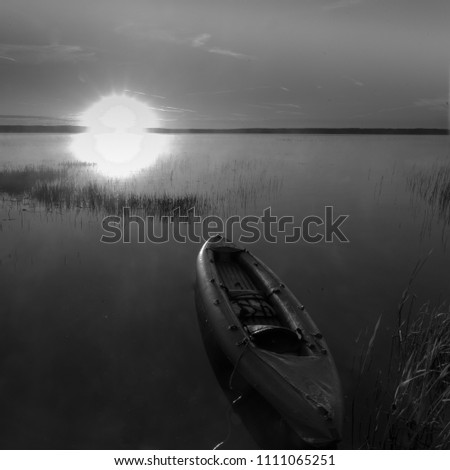 The kayak floats towards the sun.
nose kayaks against the background of a dawn, a quiet lake, a dark blue water surface and a blue sky. Symbol of movement towards adventure. Black and white photo
