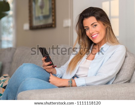 Young beautiful woman using phone on the sofa looking confident to the camera.