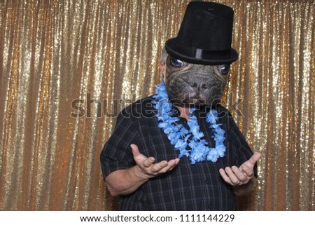 Dog Faced Boy in a Photo Booth. A man wears a Dog Face Mask and Top Hat while posing for his photo in a Photo Booth with a Gold Sequin background curtain. 
