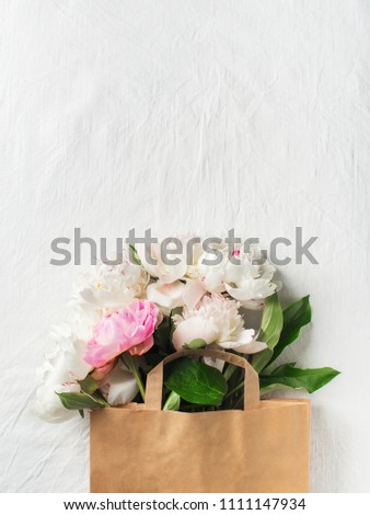 Bouquet of peonies in paper bag on white texture with copy space, mothers day, top view, flat lay