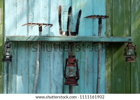 Storm lanterns and agriculture tools hanging on the old wood blue and green fence wall