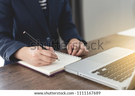 Business woman hands writing or take note on the book in office, working table and laptop, business concept