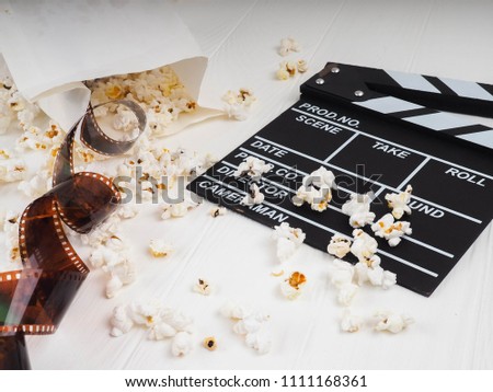 the film in the spiral, near the popcorn, Clapperboard copy space for text, fashion highlights in the photo, concept, film industry, film, abstract composition of movie, on a white background.