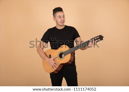 Young man holds the guitar playing music on orange background.