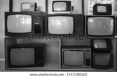 shelf near wooden wall with many vintage, aged, used  TV - television receiver