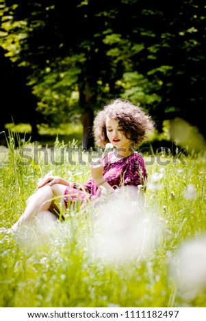 Cute girl sits on a grass with a dandelion in her hand