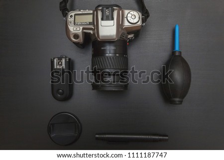 Top view of work space photographer with dslr camera system, camera cleaning kit, lens and camera accessory on black table background. Hobby journalism photography technology art concept