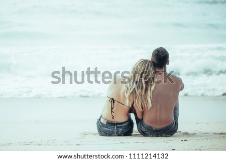 Rear view of happy young Caucasian couple sitting together on seashore
