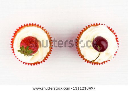 Two red cupcakes with white cream decorated with strawberry and cherry on white background. Top view. Picture for a menu or a confectionery catalog. 