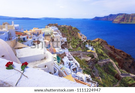 Oia town on Santorini island, Greece. Traditional and famous houses and churches with blue domes over the Caldera, Aegean sea with a pair of red roses