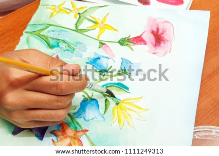 Girl draws beautiful wildflowers on white paper.