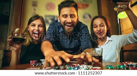 Side view photo of male and female friends sitting at wooden table. Men and women playing card game. Hands with alcohol close-up. Poker, evening entertainment and excitement concept